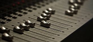 Close-up of a sound mixer board with various knobs and sliders.