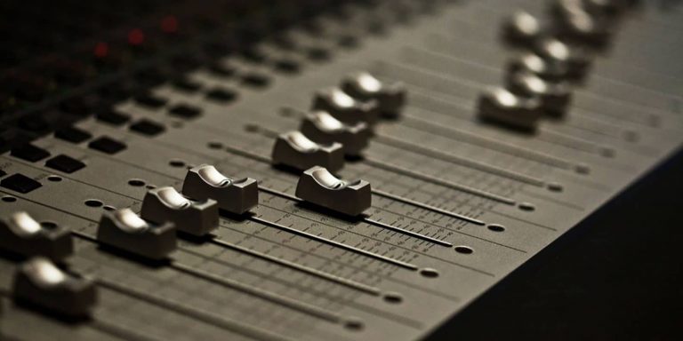 Close-up of a sound mixer board with various knobs and sliders.