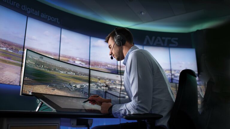 Operator managing airport operations using multi-screen workstations and centralised KVM control in a mission-critical environment.