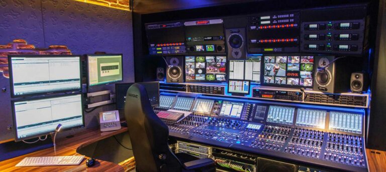 Broadcast control room with multiple screens and control panels, indoor setting with dim lighting.
