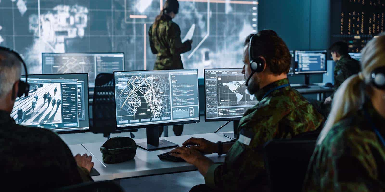 Military personnel are sitting in front of monitors and surveillance software with headsets on, in a cyber security work environment. Using highly secure IHSE Draco KVM Solutions allows instant switching, mutli-signal support and continuous operation for customized defense solutions.