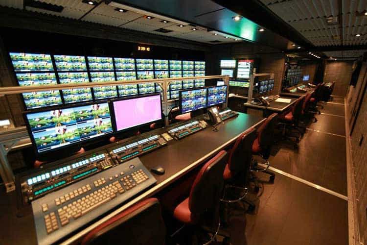 Control room featuring a KVM setup, with multiple monitors and control equipment, indoor setting with moderate lighting.