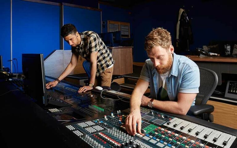 Broadcasting team operating in a studio with multiple monitors and control panels, indoor setting with professional lighting.