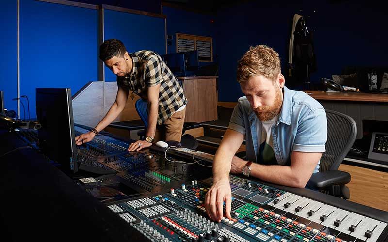 Broadcasting team operating in a studio with multiple monitors and control panels, indoor setting with professional lighting.