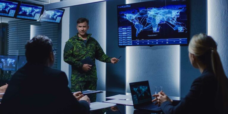 Military officer in camouflage uniform giving a security briefing in a high-tech conference room, pointing to a large screen displaying a digital world map with global network connections, while business professionals listen